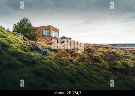 Ein winziges Haus auf einem grasbewachsenen Hügel, perfekt für einen isolierten Urlaub oder einfach nur einen ruhigen Urlaub in der Verbindung mit der Natur. Moderne Architektur in der Stockfoto