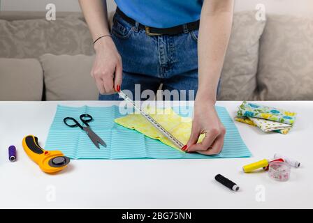 Frau in T-Shirt Maßnahmen Stoff Tuch. Es gibt Quilt-Werkzeuge auf dem Tisch. Patchwork-Messer, Schere, gefütterte Schneidematte, selbstschließend, Faden, CEN Stockfoto