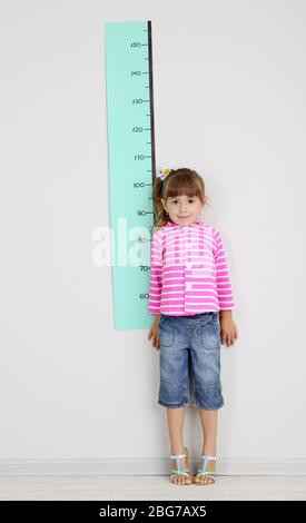 Kleines Mädchen, die Messung der Höhe gegen die Wand im Zimmer Stockfoto