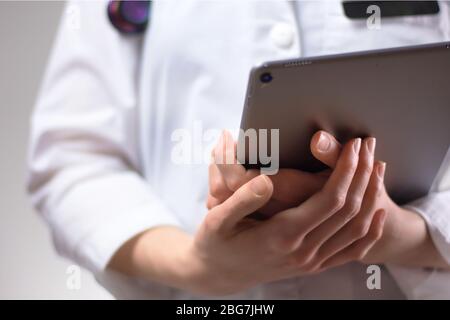 Tablet in den Händen von Gesundheitsexperten aus nächster Nähe. Weißes Fell, Stethoskop und Abzeichen im Hintergrund sichtbar. Hände eines Pflegefachpersonals oder PA U Stockfoto