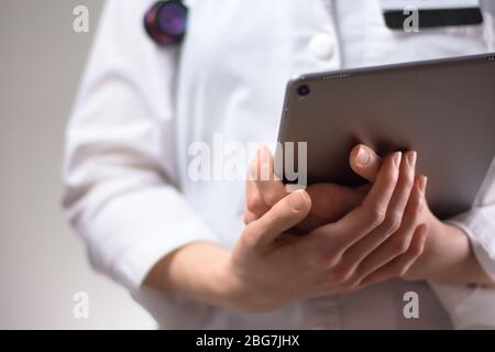 Tablet in den Händen von Gesundheitsexperten aus nächster Nähe. Weißes Fell, Stethoskop und Abzeichen im Hintergrund sichtbar. Hände eines Pflegefachpersonals oder PA U Stockfoto