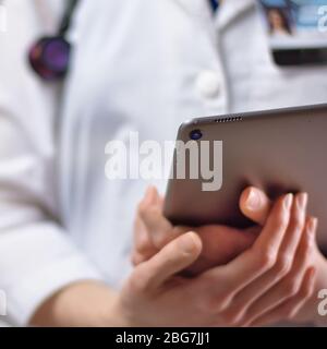 Tablet in den Händen von Gesundheitsexperten aus nächster Nähe. Weißes Fell, Stethoskop und Abzeichen im Hintergrund sichtbar. Hände eines Pflegefachpersonals oder PA U Stockfoto