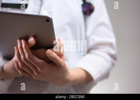 Tablet in den Händen von Gesundheitsexperten aus nächster Nähe. Weißes Fell, Stethoskop und Abzeichen im Hintergrund sichtbar. Hände eines Pflegefachpersonals oder PA U Stockfoto