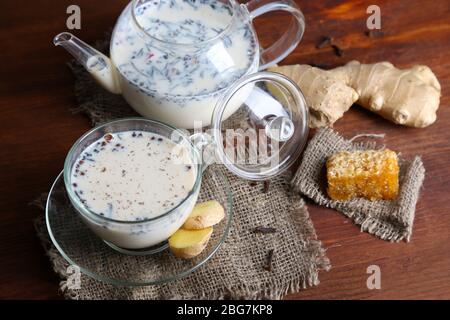 Teekanne und Tasse Tee mit Milch und Gewürzen auf Sack von Holztisch Stockfoto