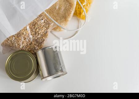 Verschiedene Dosengerichte, Pasta, Reis und rohe Getreidekörner auf einem Tisch in Papiertüte mit Kopierplatz. Spende oder Einkaufstasche mit Lebensmitteln vom Markt Stockfoto