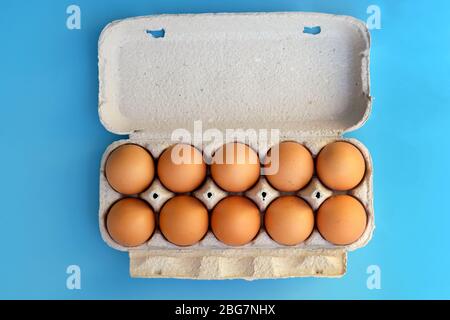 Pappschale für zehn Eier von oben. Hühnereier in einer Papierbox auf blauem Hintergrund braun werden. Eier in einem Papierbehälter. Stockfoto