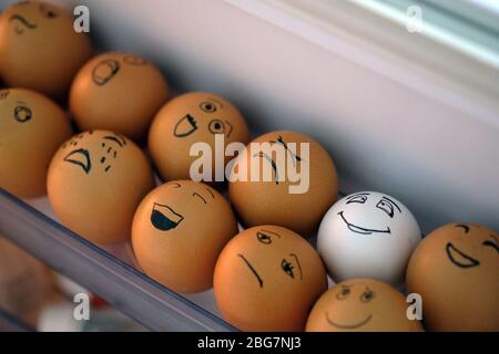 Eier im Kühlschrank in einem Plastikbehälter. Eieraufbewahrung im Kühlschrank auf einem Regal an der Tür. Eier mit emotionalen Gesichtern bemalt. Weiß und Stockfoto