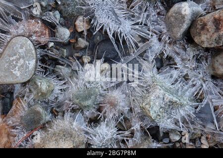 Bunte Felsen umgeben von sternenartigen Eisformationen in einem kleinen Bach Stockfoto