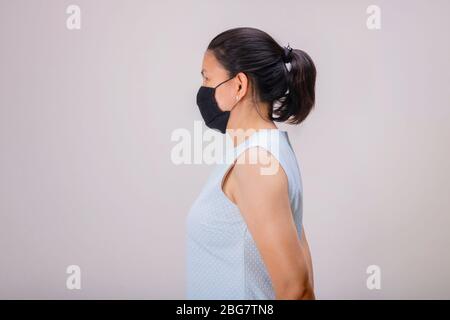 Ein asiatisches Mädchen in blauem Tank Top trägt schwarze Maske, während sie ihr eigenes Haar zieht. Stockfoto