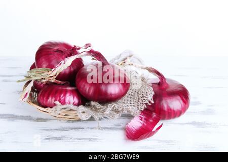 Frische rote Zwiebeln in Korbkorb auf Holztisch auf weißem Hintergrund Stockfoto