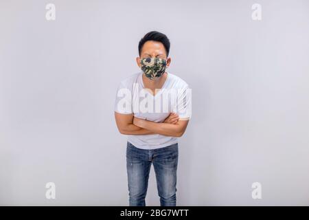 Ein asiatischer Kurzhaarmann in weißer Casual und Jeans posiert vor der Kamera in der Studiobeleuchtung, während er Tarnmaske trägt Stockfoto