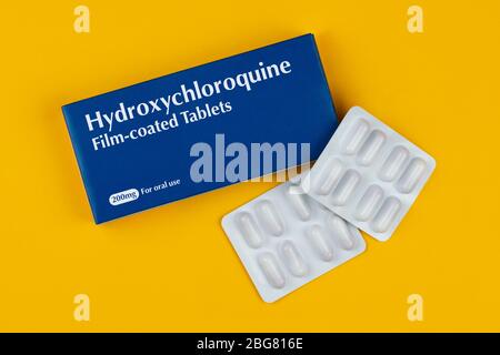 Eine Schachtel Tabletten mit der Aufschrift Hydroxychloroquin schoss vor gelbem Hintergrund. Stockfoto