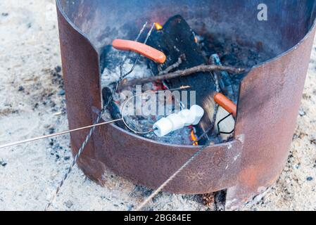 Nahaufnahme von Hot Dogs und Marshmallows, die auf Röstersticks über dem Lagerfeuer kochen Stockfoto
