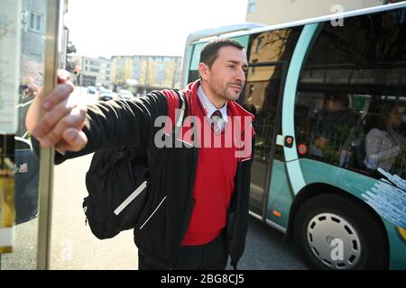 Friedrichshafen, Deutschland. April 2020. Zoran Djuric, Busfahrer des Regionalverkehrs Alb-Bodensee (RAB), steht nach dem Fahrerwechsel an der Bushaltestelle, während im Hintergrund ein Bus abfährt. (An dpa: ''Wir haben wenige Kontakte' - als Busfahrer während der Corona-Zeiten unterwegs') Quelle: Felix Kästle/dpa/Alamy Live News Stockfoto