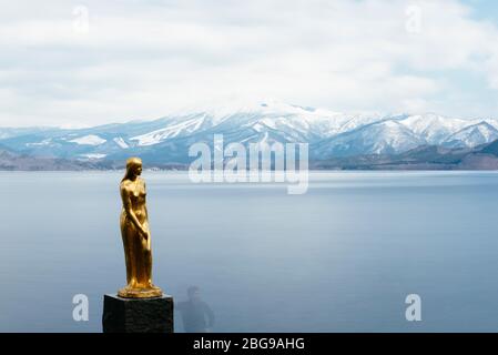 Eine goldene Statue von Tatsuko steht gegen das majestätische Wasser des Tazawa Sees. Stockfoto