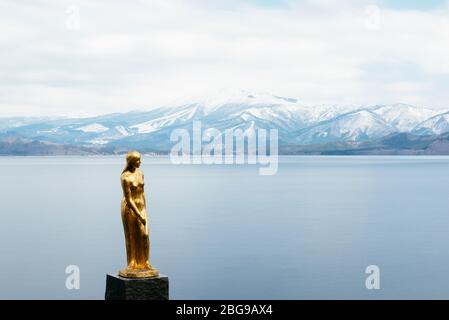 Eine goldene Statue von Tatsuko steht gegen das majestätische Wasser des Tazawa Sees. Stockfoto