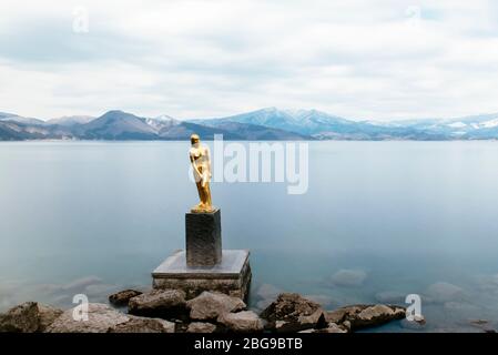 Eine goldene Statue von Tatsuko steht gegen das majestätische Wasser des Tazawa Sees. Stockfoto