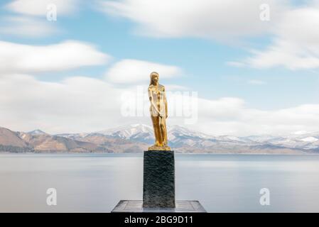 Eine goldene Statue von Tatsuko steht gegen das majestätische Wasser des Tazawa Sees. Stockfoto