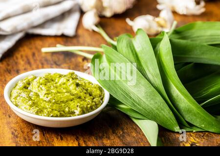 Bärlauch-Pesto und grüne Ramsons-Blätter auf Holztisch. Stockfoto