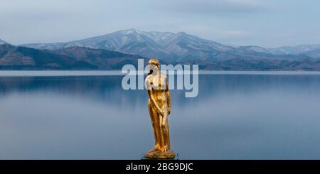 Eine goldene Statue von Tatsuko steht gegen das majestätische Wasser des Tazawa Sees. Stockfoto