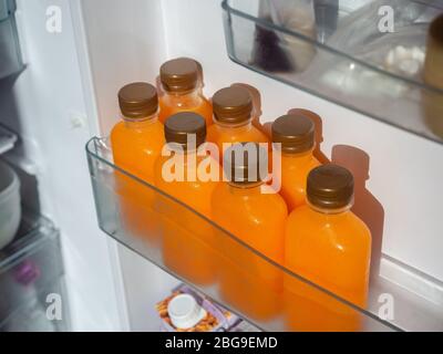 Orangensaft war kalt in den Flaschen auf dem Regal im Kühlschrank. Quadratische Flasche mit kaltem Orangensaft, Draufsicht. Stockfoto