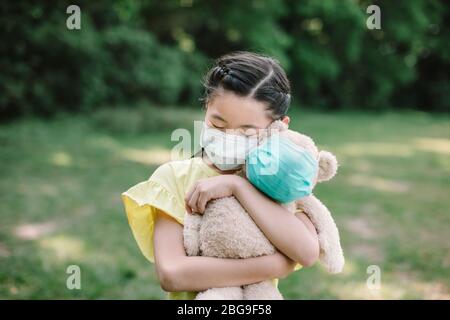 Stress asiatische kleine Mädchen Holding Spielzeug Bär tragen medizinische Schutzmaske Stockfoto