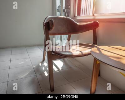 Sessel aus Holz im Retro-Stil mit Sitzkissen aus braunem Leder und Holztisch in der Nähe des Fensters in weißem Raum. Stockfoto