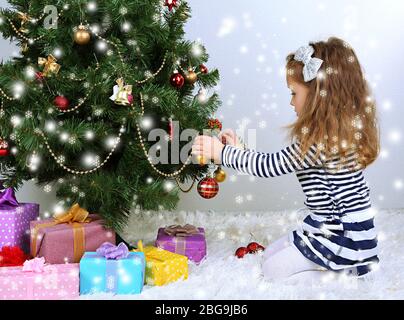 Kleines Mädchen schmücken Weihnachtsbaum mit Kugeln im Zimmer Stockfoto