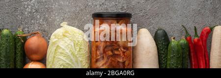 Panorama-Aufnahme von Chilischoten, Gurken, Daikon Rettich, chinakohl, Zwiebeln und Kimchi-Glas auf grauem Beton Hintergrund Stockfoto