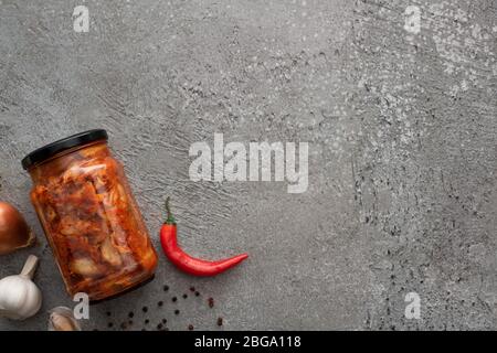 Draufsicht auf Kimchi-Glas, Chili und Knoblauch auf Betonoberfläche Stockfoto