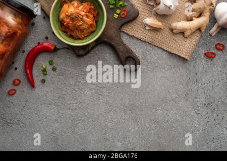 Draufsicht von Kimchi in Schüssel und Glas in der Nähe von Chili Pfeffer, Knoblauch und Ingwer auf Betonoberfläche Stockfoto