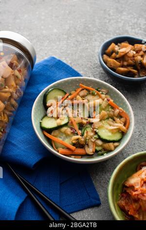 Köstliche Kimchi in Schüsseln und Glas in der Nähe Essstäbchen auf blauem Tuch auf Betonoberfläche Stockfoto