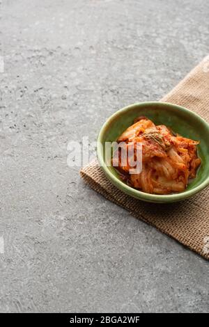 Schale mit leckeren koreanischen Kimchi und Sacktuch auf Betonoberfläche Stockfoto