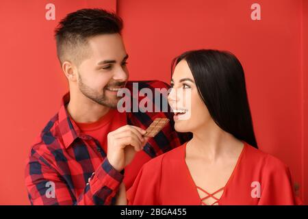 Schönes junges Paar mit leckeren Schokolade auf farbigen Hintergrund Stockfoto