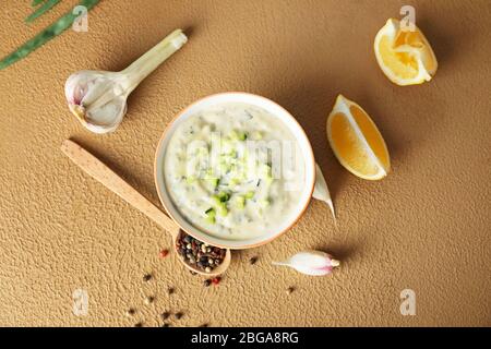 Köstliche Joghurt-Sauce mit Gurke in Schüssel auf farbigen Hintergrund Stockfoto