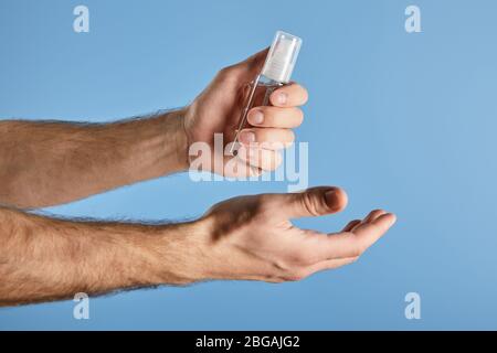 Zugeschnittene Ansicht des Mannes, der Handdesinfektionsmittel in einer Sprühflasche auf Blau hält Stockfoto