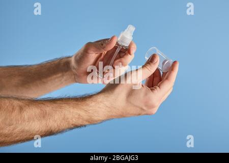 Zugeschnittene Ansicht des Mannes, der Handdesinfektionsmittel in einer Sprühflasche auf Blau hält Stockfoto
