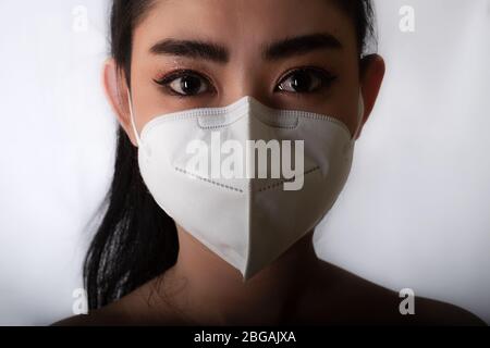 Nahaufnahme der jungen Asienfrau, die eine medizinische Maske n95 aufsetzt, um vor Atemwegserkrankungen wie der Grippe-covid-19 PM2.5 Staub und Smog bei gr Stockfoto