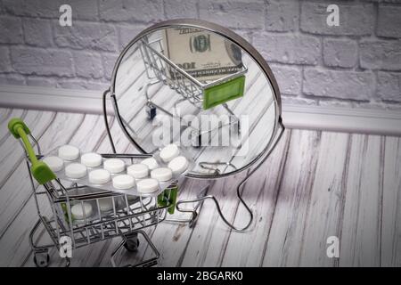 Pillen in einem Einkaufswagen. Reflexion im Spiegel von hundert Dollar Stockfoto