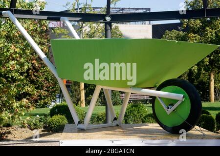 Übergroße grüne, neue und leere Schubkarre Einsatz für Garten oder Bau auf einer Plattform angezeigt. Gartenbau oder Bauwerkzeug . Stockfoto