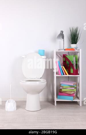 Weiße Toilettenschüssel und Ständer mit Büchern, auf farbigen Wandhintergrund Stockfoto