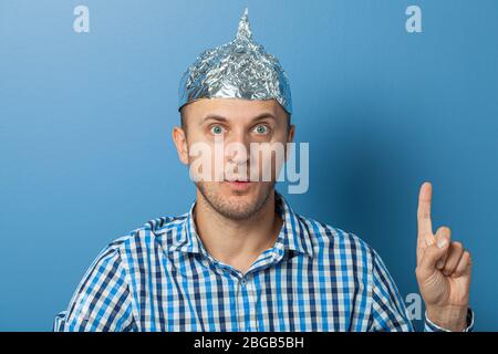 Folienhut auf Mann. Mann mit einem überraschten Gesicht zeigt Daumen nach oben. Schützt vor dem Lesen denken. Stockfoto