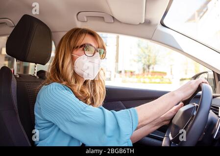 Aufnahme einer Frau mittleren Alters, die während der Coronavirus-Pandemie mit dem Auto eine Gesichtsmaske trägt. Stockfoto