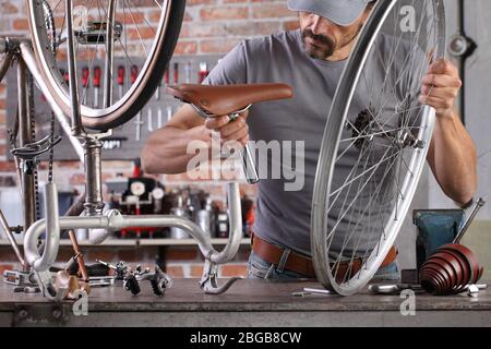 Mann reparieren das Vintage-Fahrrad in der Werkstatt auf der Werkbank mit Werkzeugen, diy-Konzept Stockfoto