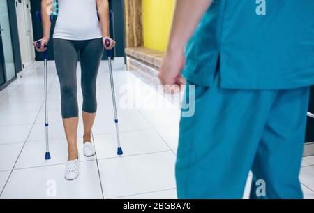 Patientin, die Krücken zur Rehabilitation nach Verletzungen verwendet. Physiotherapeut, der einen Patienten unterstützt. Stockfoto