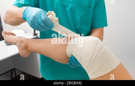 Knieverbandungsprozess des Patienten mit elastischer Bandage zur Fixierung des Kniegelenkes in fixierter Position. Physiotherapeut Bandage Knie Nahaufnahme Stockfoto