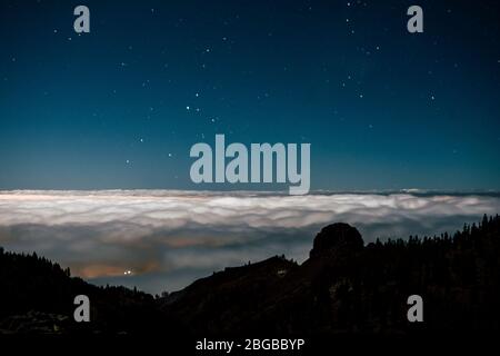 Nachtansicht der schönen blauen Landschaft mit Bergen in Silhouette und Nachtlicht am Himmel mit Sternen und weißen Wolken im Hintergrund Stockfoto