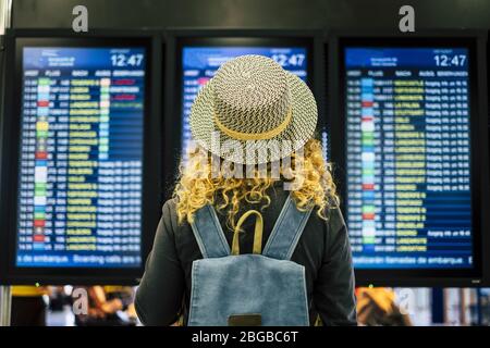 Reiseleute im Flughafen oder Bahnhof Konzept - Blick von hinten von einer blonden lockigen Frau mit blauen Rucksack suchen und überprüfen Zeit departtu Stockfoto