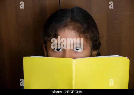 Schulmädchen bedeckte ihr Gesicht mit Buch Stockfoto