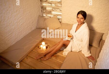 Schöne Mulatto Frau genießt Entspannung in einem Salzzimmer bei Kerzenlicht mit einer Tasse Tee in den Händen Stockfoto